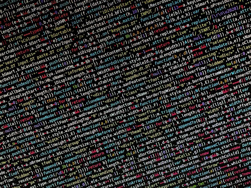 A close-up photograph of a computer screen displaying lines of colorful programming code, including various syntax elements like functions, variables, and conditionals in shades of red, green, blue, y